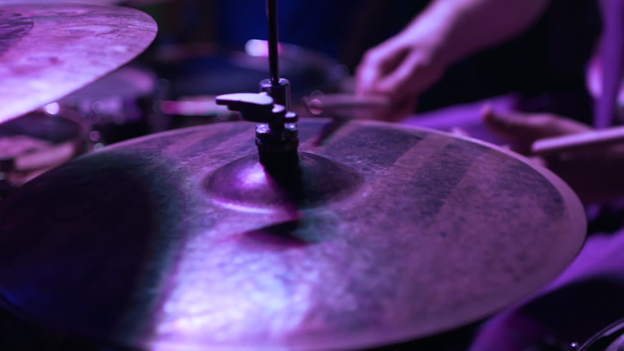 Primo piano di un batterista che suona i piatti sotto luci di scena viola