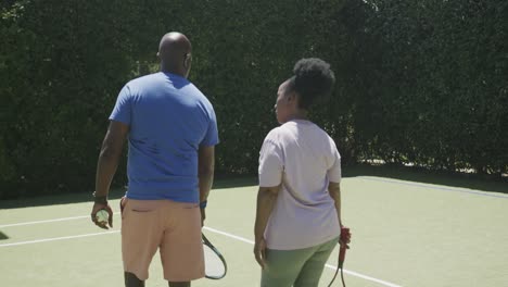 Glückliches-älteres-Afroamerikanisches-Paar,-Das-In-Zeitlupe-Mit-Tennisschlägern-Auf-Dem-Tennisplatz-Läuft