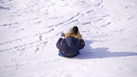 boy sledging down the hill. ice slide at winter park. happy kid riding on a plastic plate on snow.