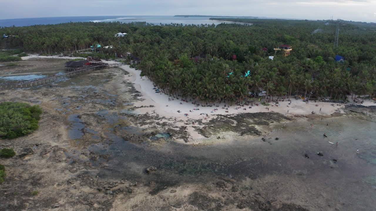 Dron ascendiendo hacia una pequeña playa con grupos de personas relajándose en una isla tropical.