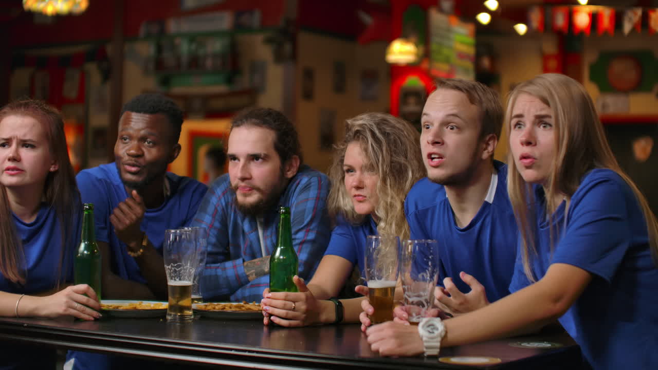 fanáticos emocionales en camisetas azules en el bar de cerveza. grupo multiétnico de personas afroamericanas están molestos y tristes debido al fracaso de su equipo