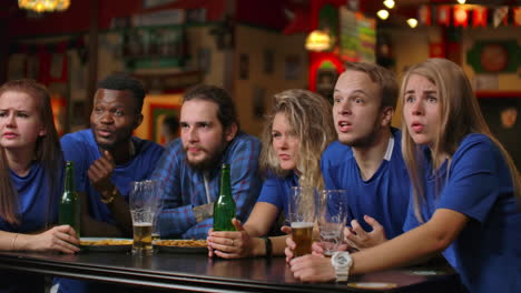 emotional fans in blue t-shirts at the beer bar. multi-ethnic group of african-american people are upset and sad because of the failure of their team