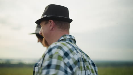 close-up of a joyful couple running through a grassy field at sunset, smiling . the man is styled in a black hat and checkered shirt, and the woman in a white dress with a matching hat