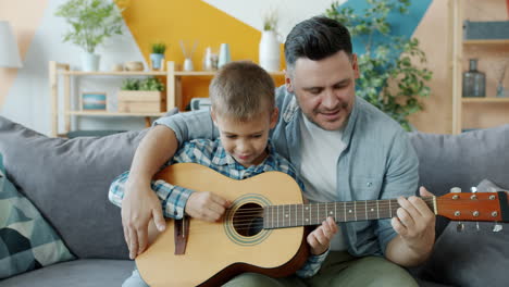 father and son learning to play guitar together at home