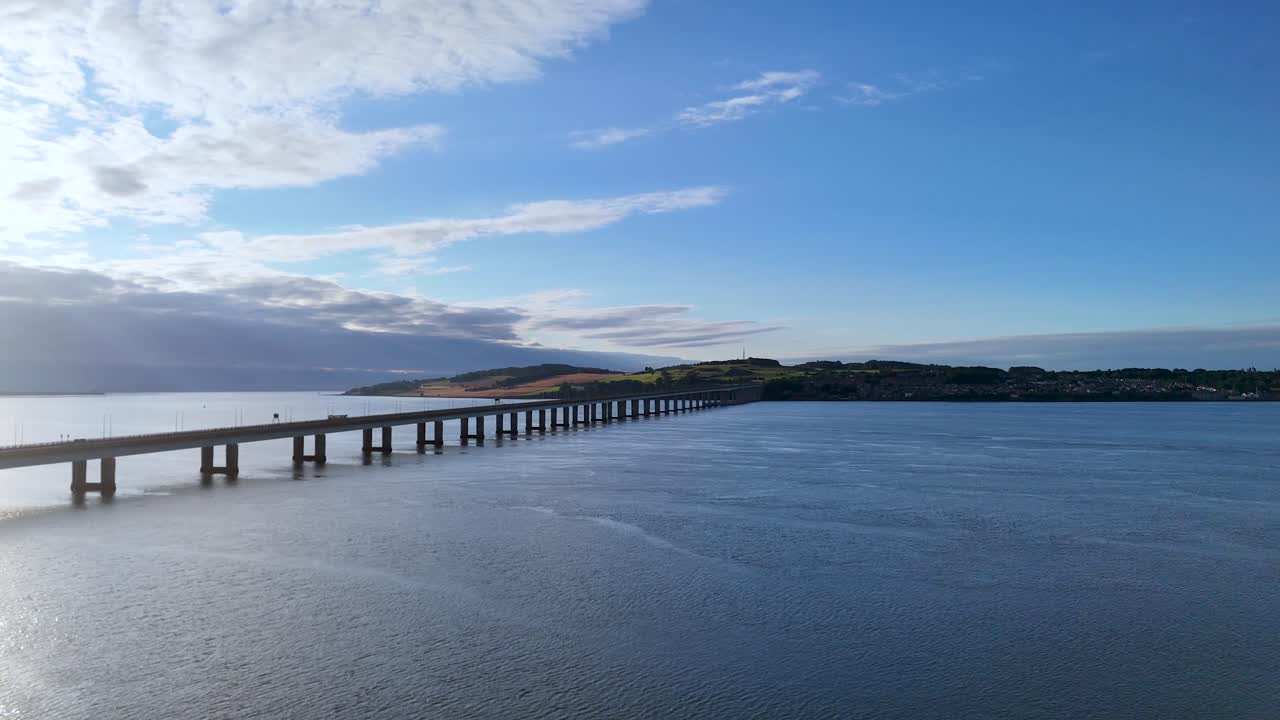 Sweeping aerial footage captures a long bridge crossing a wide river under bright daylight, with gentle camera movement and expansive sky above Inverness