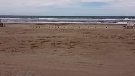 aerial flight over sandy beach towards atlantic ocean during cloudy day - empty beach with stormy waves in backdrop