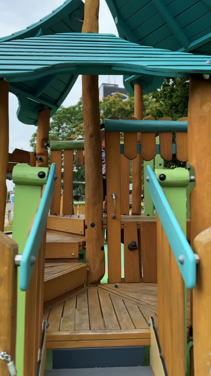 Toddler kid goes up by the wooden stairs on all four. Baby boy plays at the playground in summer. Vertical video.