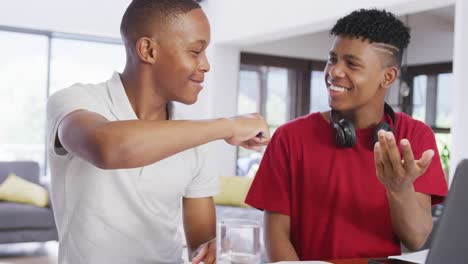 Three-happy-diverse-male-teenage-friends-using-laptop-and-talking-at-home,-slow-motion