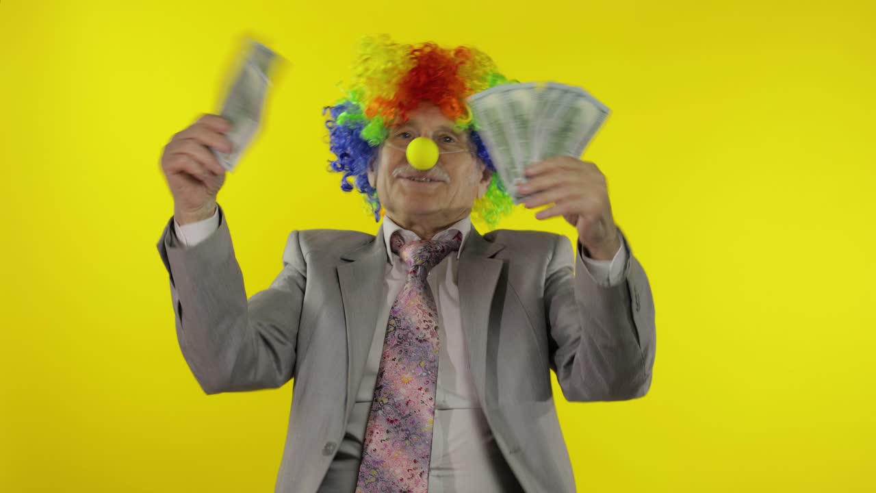 Elderly clown businessman entrepreneur boss dancing with money cash banknotes