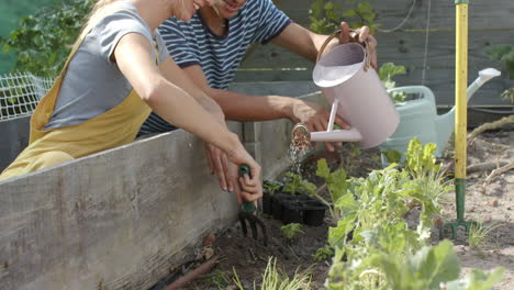 Feliz-Pareja-Diversa-Trabajando-En-El-Jardín-Y-Regando-Plantas,-Cámara-Lenta