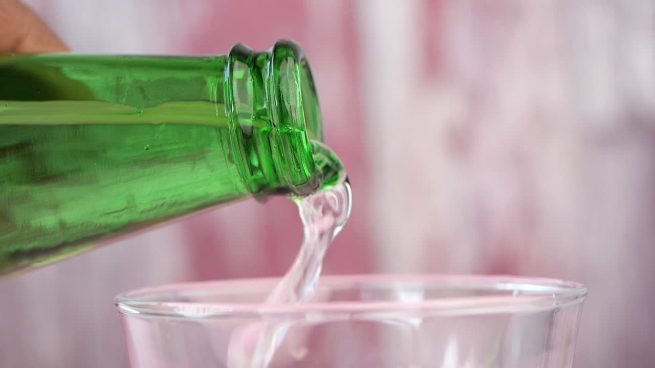 Pouring water from a green bottle into a glass