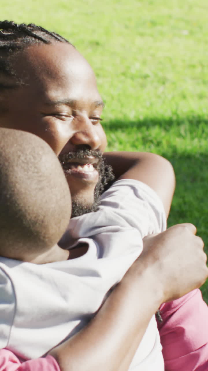 video de un feliz padre e hijo afroamericanos haciendo picnic en la hierba y abrazándose