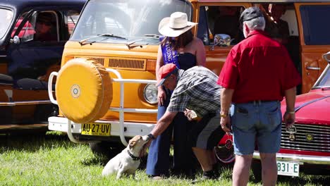 people interacting with a dog near vintage cars