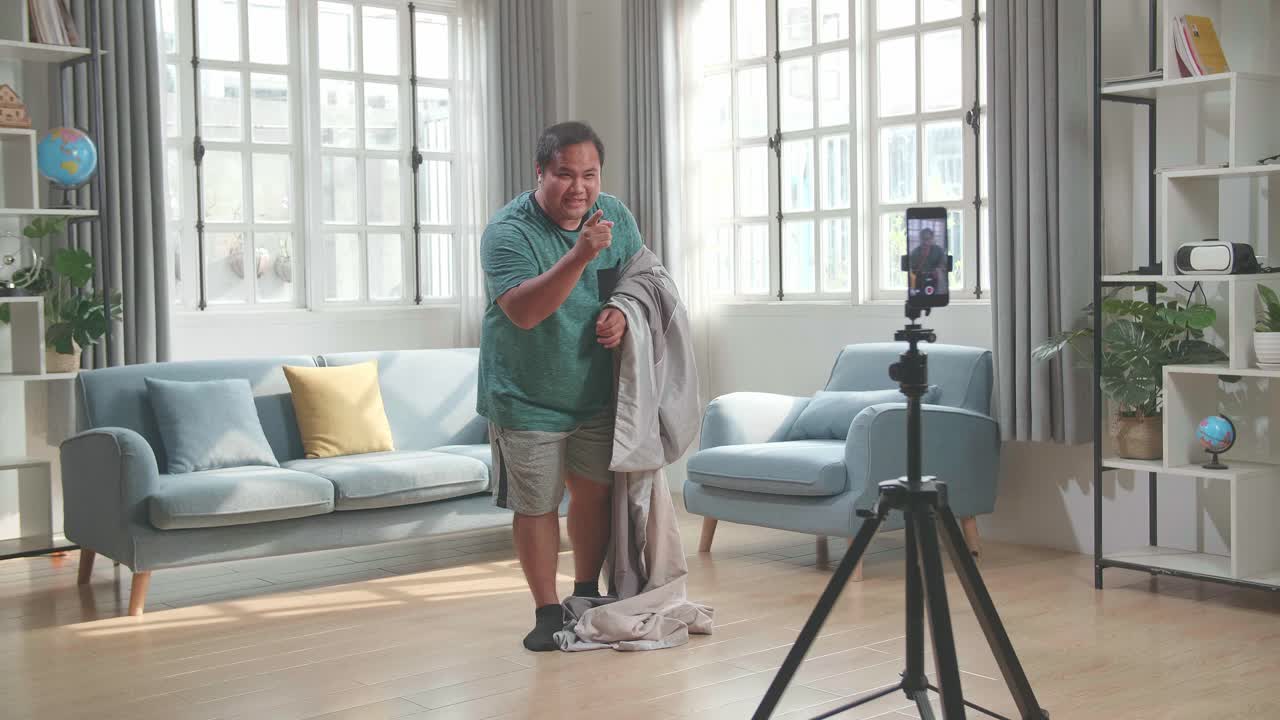 Asian Man Shows Trick With Disappearing On Mobile Phone Camera While Recording On Smartphone Video Content For Social Networks In Cozy Room