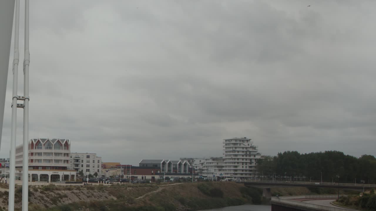 Overcast day, people walk across contemporary bridge toward urban waterfront, steady forward camera movement