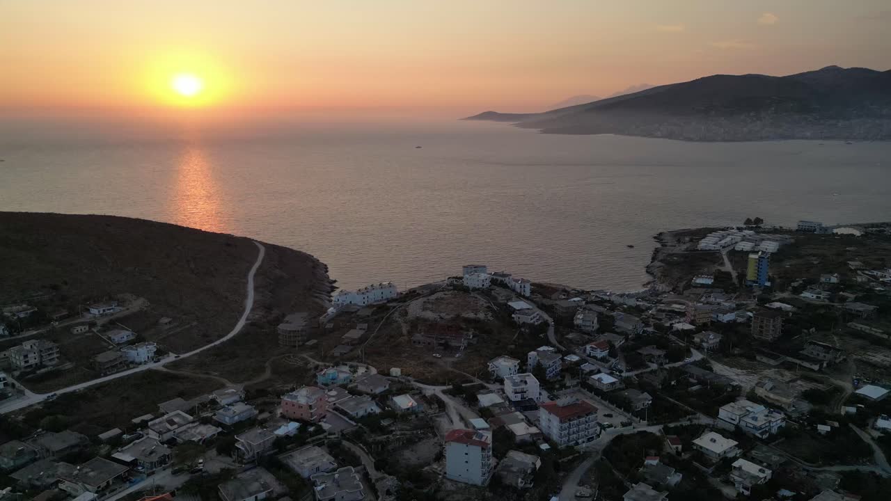 A breathtaking drone capture of a vibrant sunset over the oceanic horizon, casting warm hues over waterfront homes, creating a serene and picturesque scene.