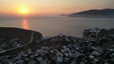 a breathtaking drone capture of a vibrant sunset over the oceanic horizon, casting warm hues over waterfront homes, creating a serene and picturesque scene.