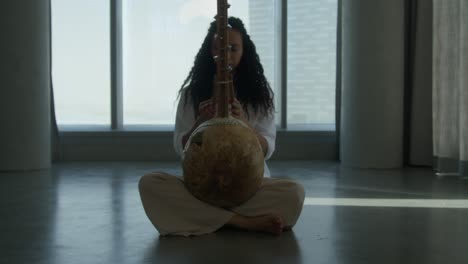 wide shot of a girl playing kora strings percussion african harp, backlit shot, sun rays coming through the windows