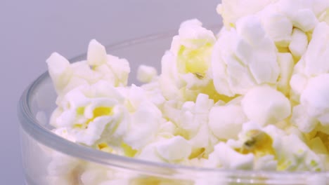 Golden-and-fatty-popcorn-in-a-transparent-glass-bowl,-rotating