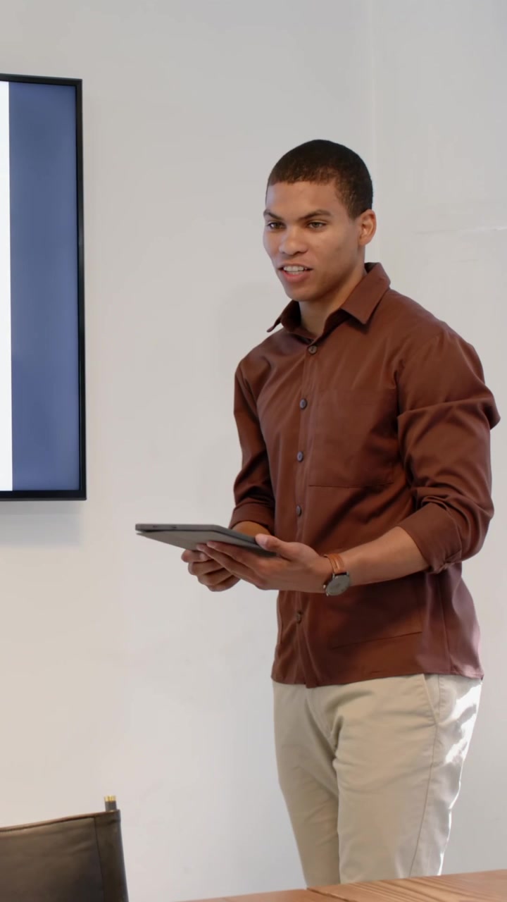 Video verticale: Uomo afroamericano che presenta in una sala riunioni, tocca il tablet e indica lo schermo