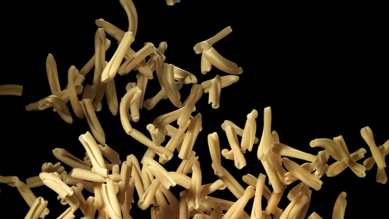 Pasta casarecce cruda che cade al rallentatore su sfondo nero.