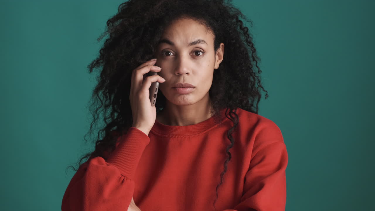 una mujer afroamericana seria usando un teléfono inteligente sobre un fondo azul.