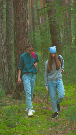 las mujeres recuperan sus bolsas en un bosque pacífico, preparándose para continuar su caminata, con árboles altos y vegetación exuberante que los rodean, cuelgan sus bolsas sobre sus hombros, se alejan
