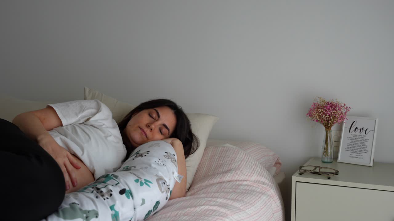 Pregnant woman in bed taking glasses off to sleep. Lights gradually dim