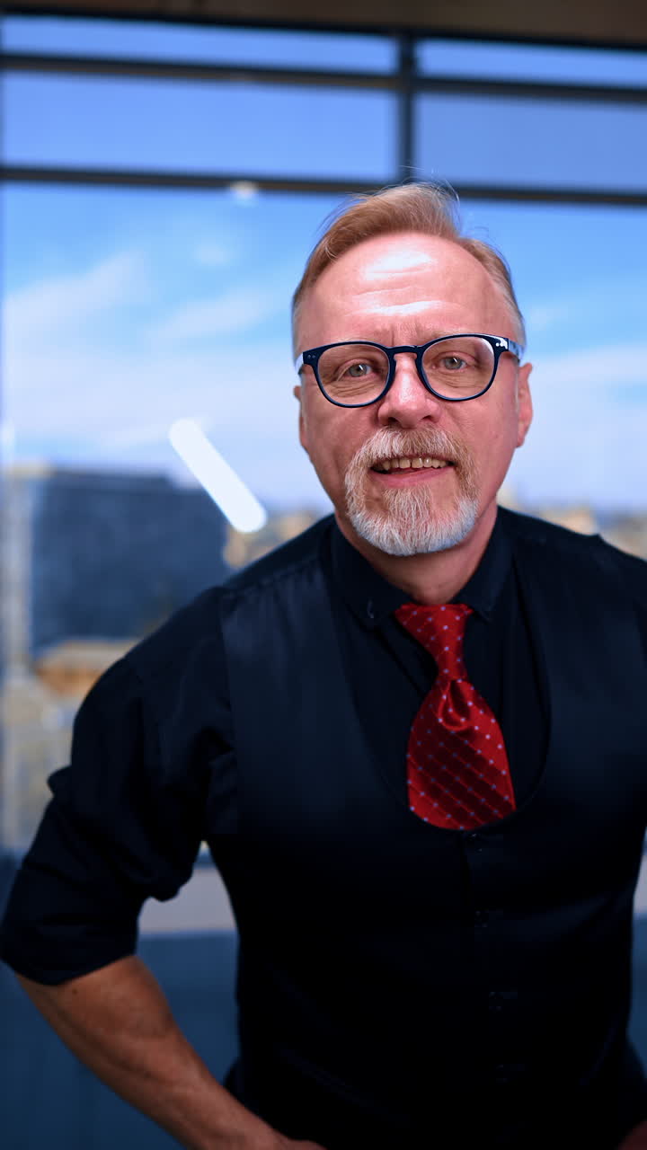 Adult male wearing black shirt, vest and red tie males a slot with his hands peeping through it to the camera. Portrait of a Caucasian man in glasses joking. Vertical video.