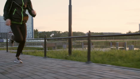 woman in sportswear running along city riverside promenade in the morning at sunrise