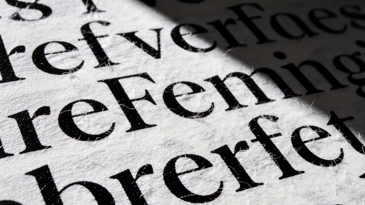 Shifting off-frame light casting diagonal shadow across serif text on textured paper revealing ink