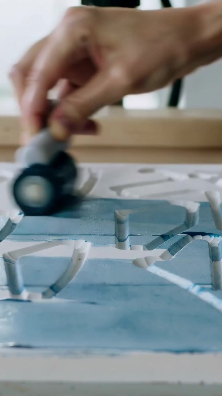 Vertical video: Grasping brayer, right hand rolling in shop, filling carved panel with blue paint