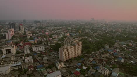 drone aéreo hacia adelante disparado sobre los edificios de la ciudad en bangkok, tailandia con cielo naranja después de la puesta de sol en el fondo