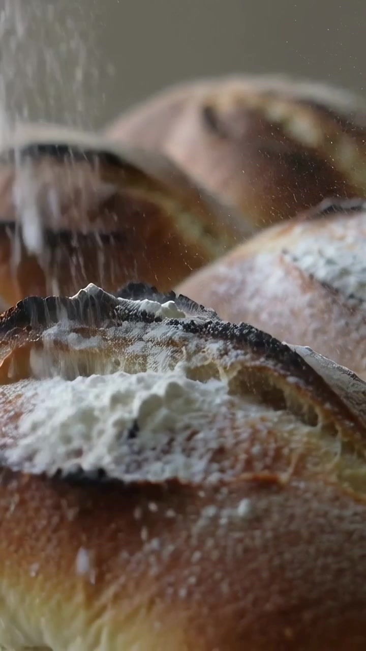 Vertical video: Falling powder dusting artisan bread loaves on baking tray, for display