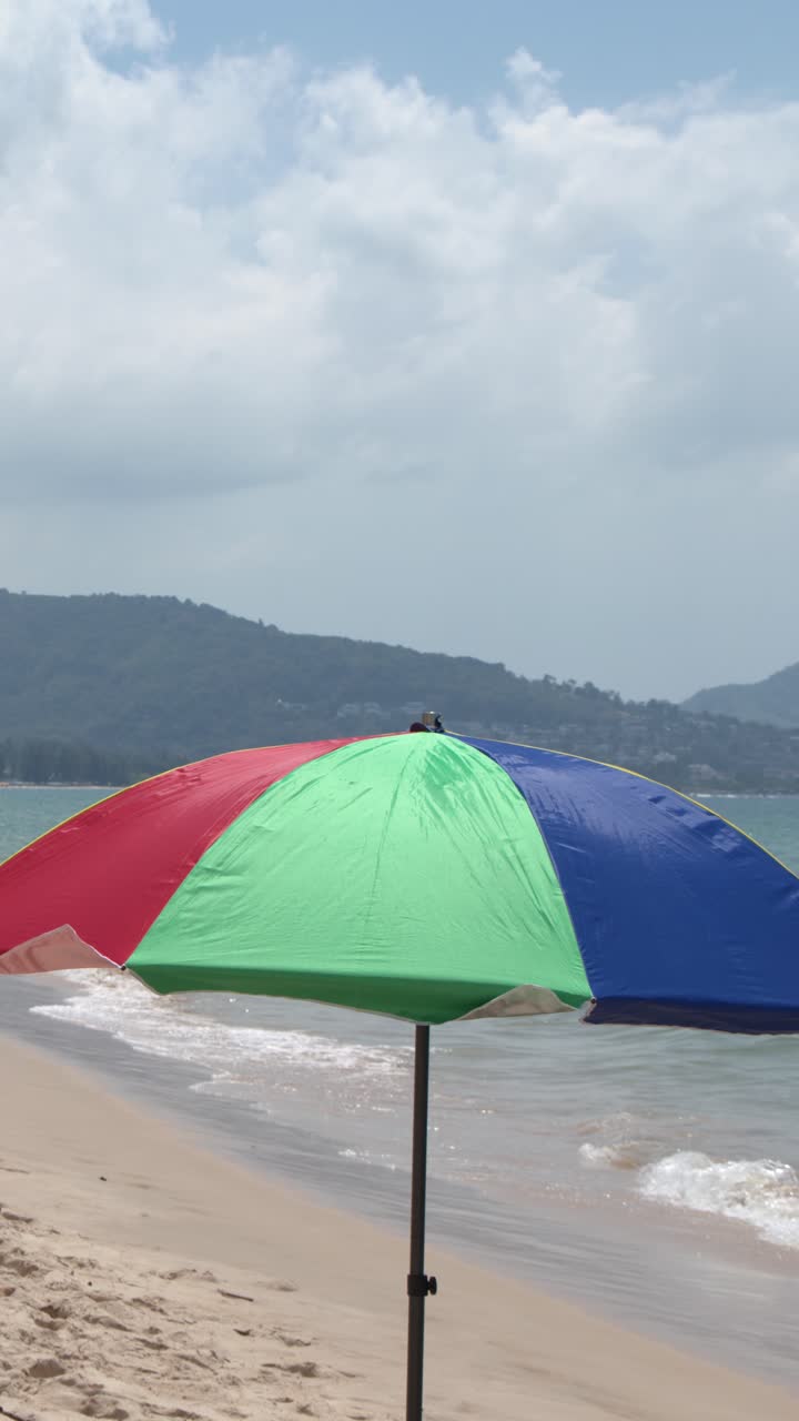 Un vivace ombrellone multicolore si erge su una spiaggia sabbiosa con dolci onde oceaniche che si infrangono.