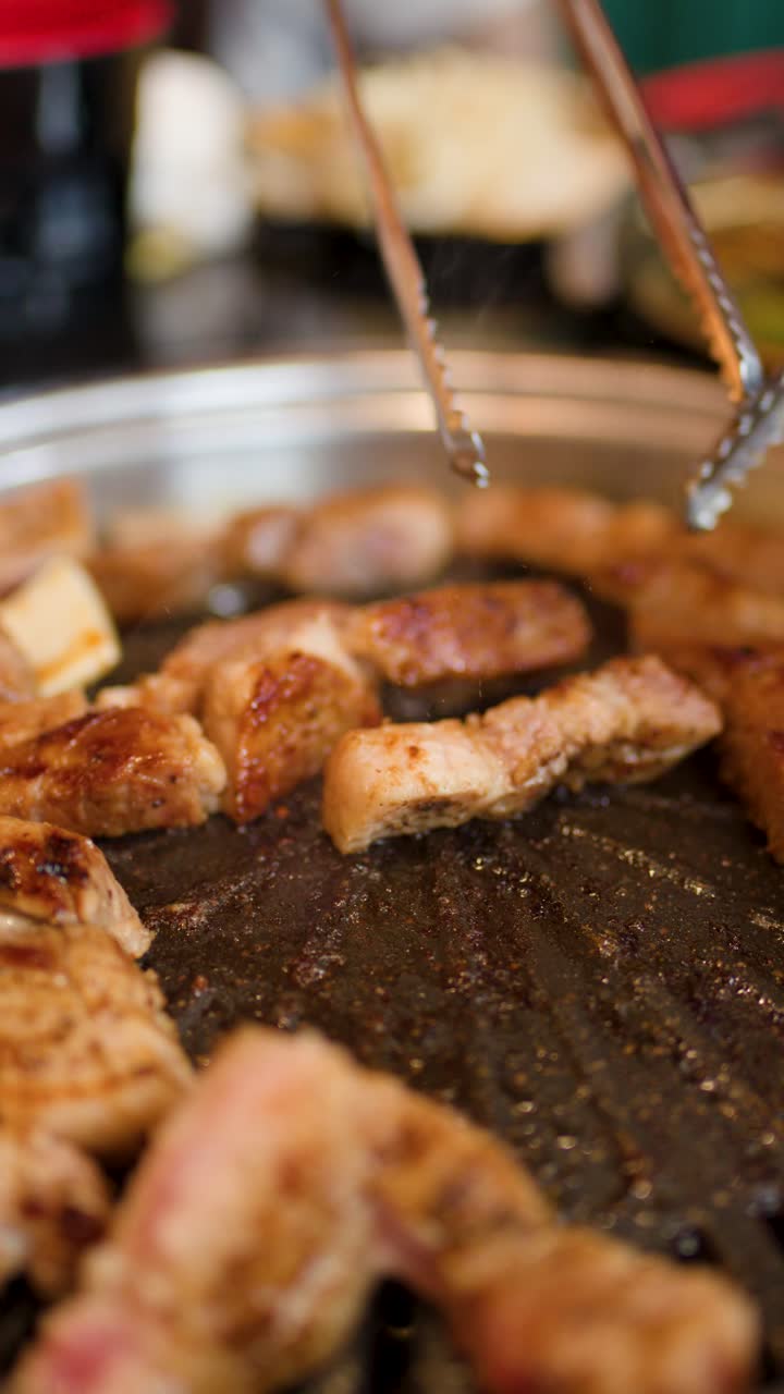 Gros plan sur des cubes de poitrine de porc juteux grésillant sur un grill de table, des pinces retournant délicatement la viande