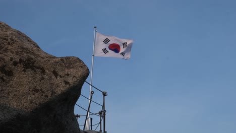 a south korean flag flies and blows in the wind on top of a mountain in asia