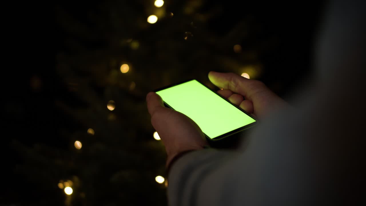 Tenendo uno smartphone con schermo verde davanti all'albero di Natale.