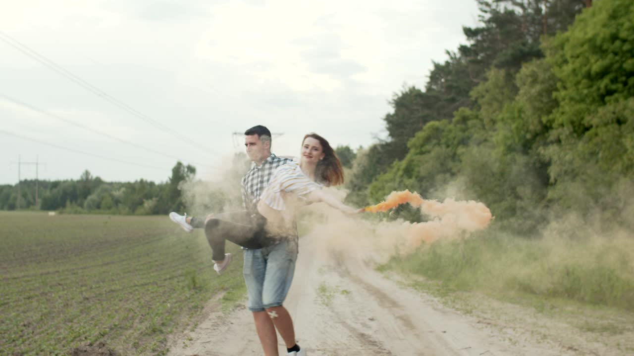 hombre dando vueltas a una mujer joven con una bomba de humo al aire libre