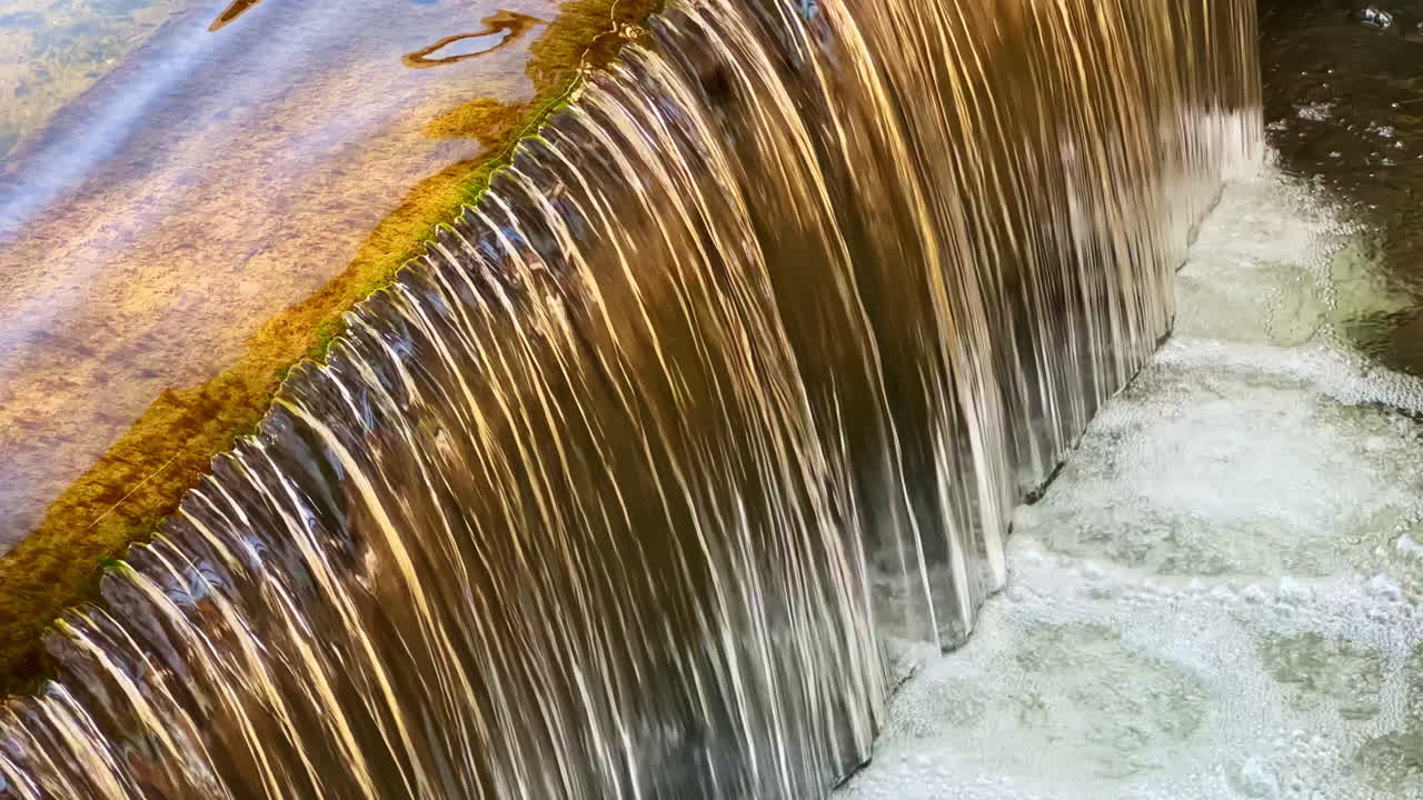 Bella cascata d'acqua che scorre su una sporgenza coperta di muschio in un ambiente naturale sereno durante un pomeriggio di sole
