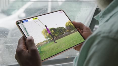 Video-of-african-american-man-sitting-on-sofa-and-watching-football-on-tablet-at-home