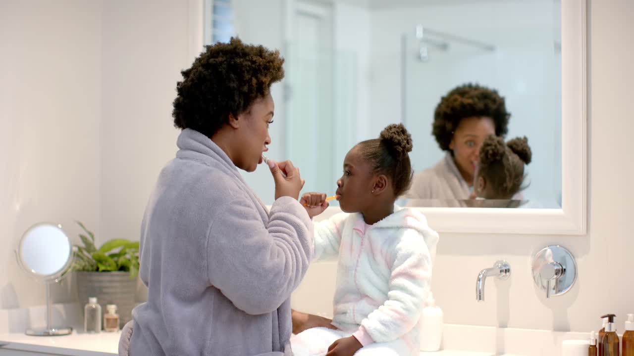Young African American mother brushes teeth with African American daughter at home