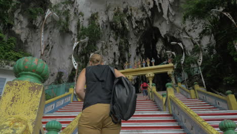 una mujer joven en las cuevas de batu, malasia, sube las escaleras y toma fotos en una tableta.