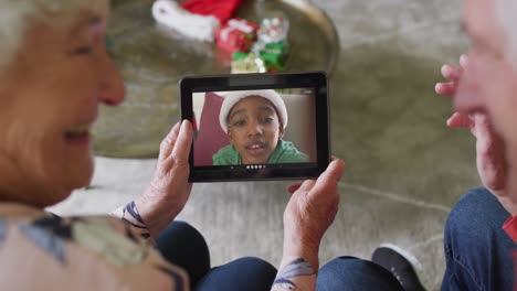 Sonriente-Pareja-Caucásica-Senior-Usando-Tableta-Para-Videollamada-Navideña-Con-Niño-En-Pantalla