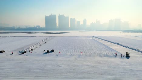pan drone shot of songhua river workers harvesting ice blocks and skyline behind in harbin, heilongjiang, china