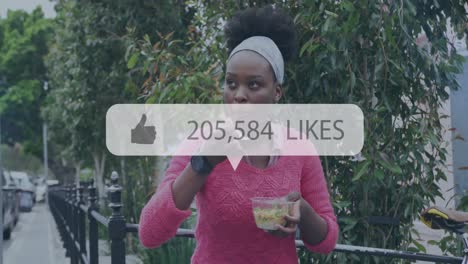 Animation-of-increasing-likes-on-speech-bubble-over-african-american-woman-having-a-snack-on-street