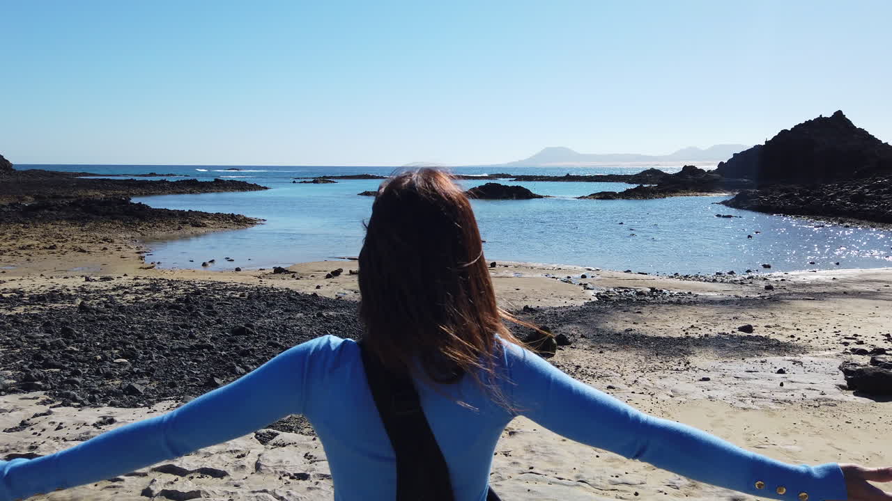 woman from behind with arms outstretched enjoying the ocean view on a sunny day on Lobos Island beach, Fuerteventura