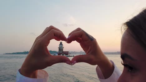 beautiful girl makes heart shape with view of maiden tower inside in istanbul, turkey