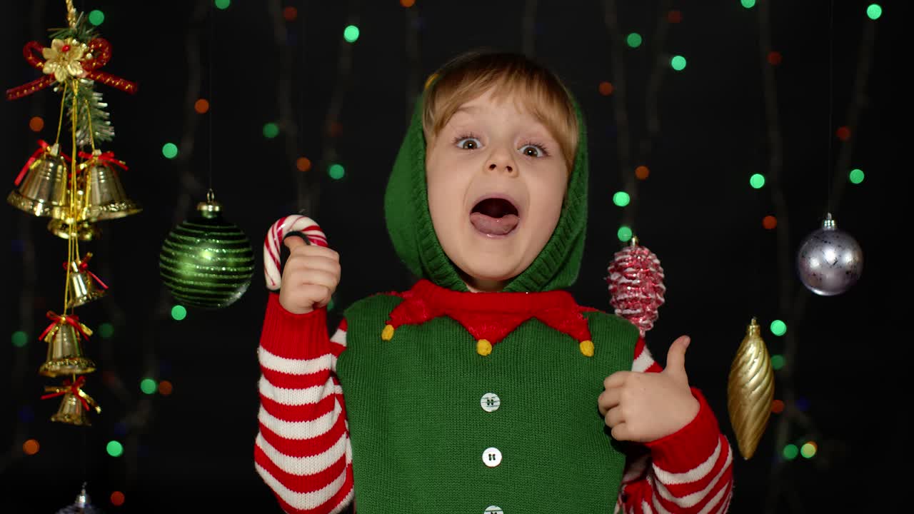 Náctiletá dívka v kostýmu vánočního elfa / pomocníka Santa Clause ukazuje palec nahoru na černém pozadí