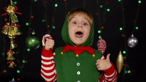 Teen-kid-girl-in-Christmas-elf-Santa-Claus-helper-costume-showing-thumbs-up-on-black-background